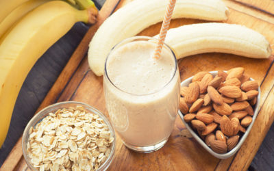 A glass of smoothie with bananas, nuts and oats on a chopping board